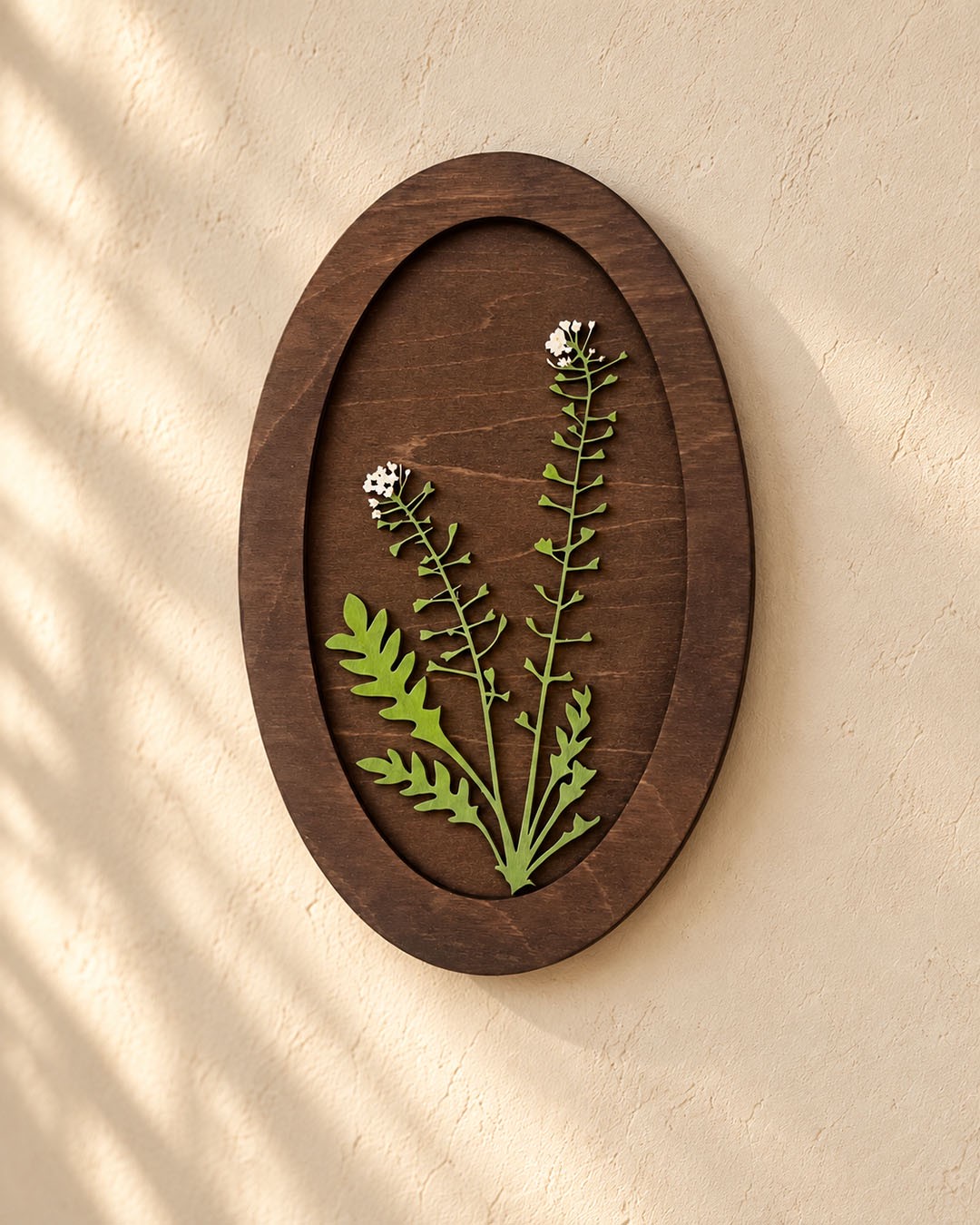 An oval dark wood panel with green stems and white flowers on a warm plaster wall