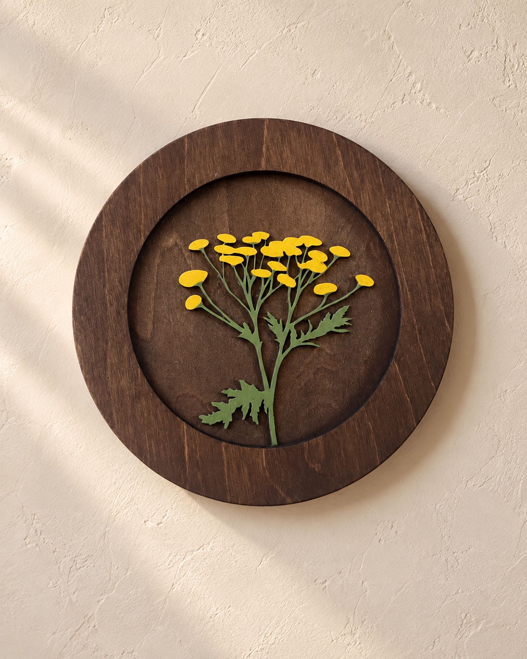 A round dark wooden panel with small yellow flowers on a pale plaster wall